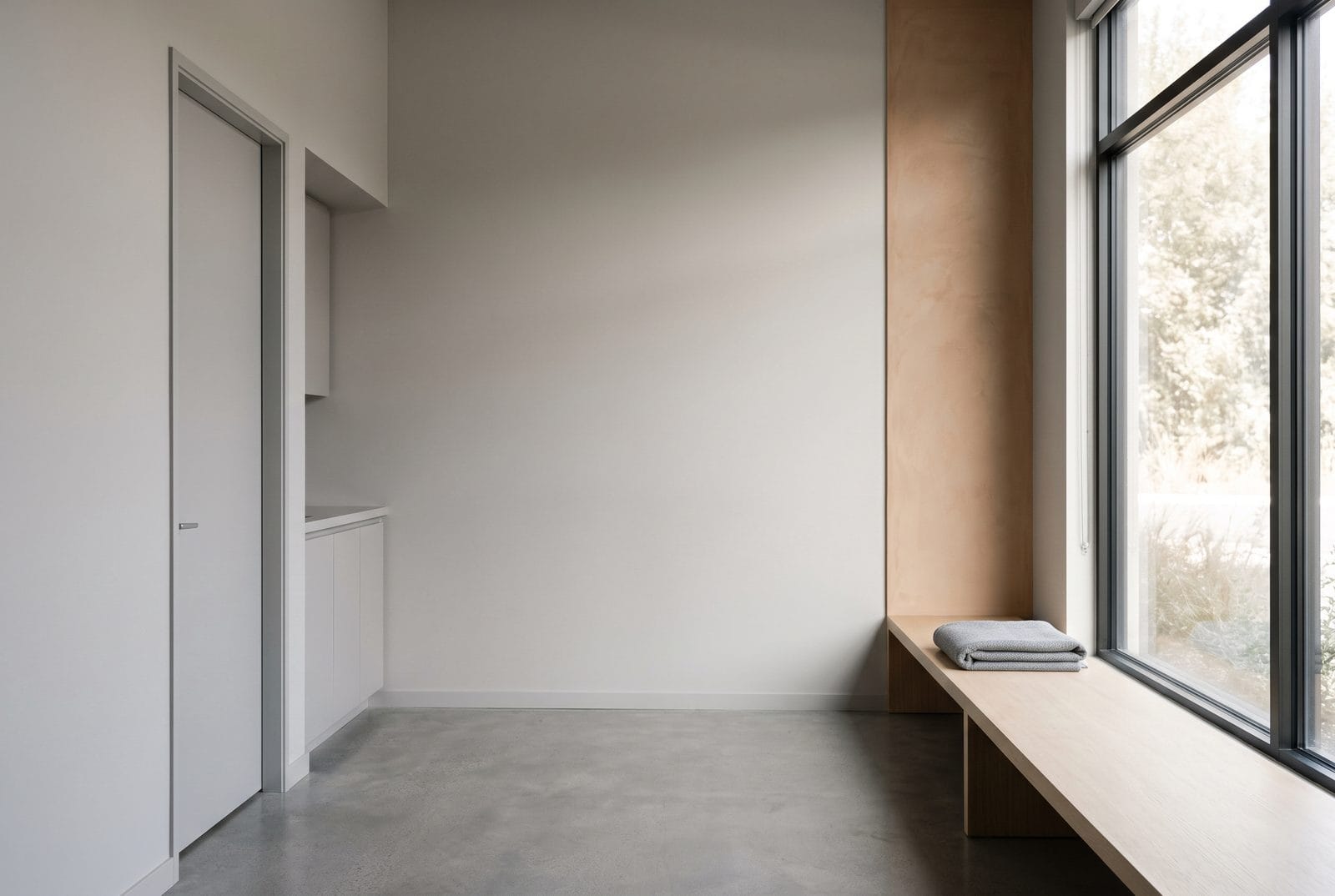 A plain timber bench beneath a tall window with a folded wool blanket on one end.