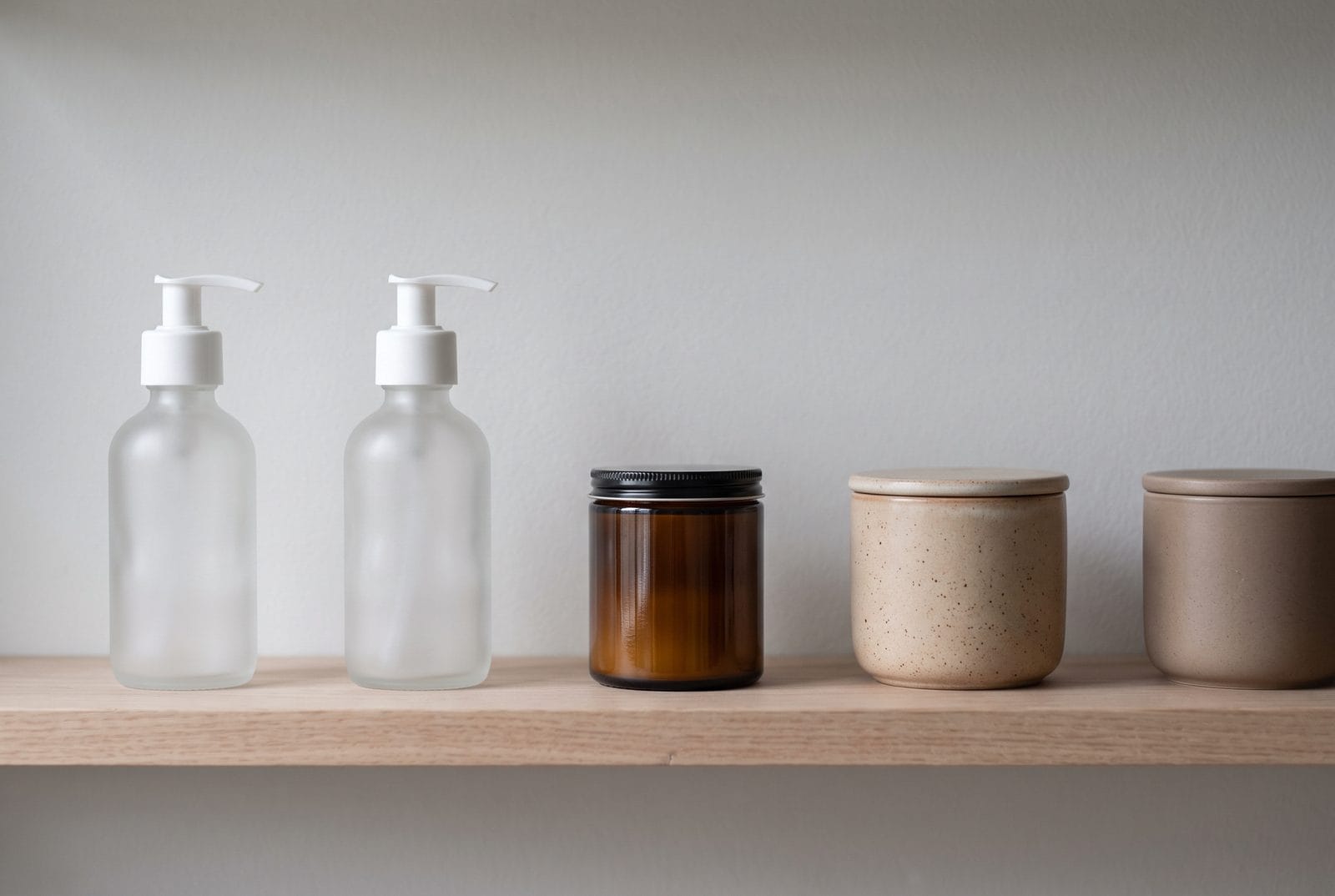 A single pale timber shelf holding five plain unlabeled vessels, evenly spaced.