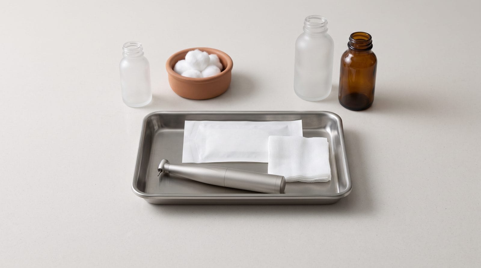 A plain matte cordless handpiece resting in a shallow stainless tray beside a sealed sterile pouch.